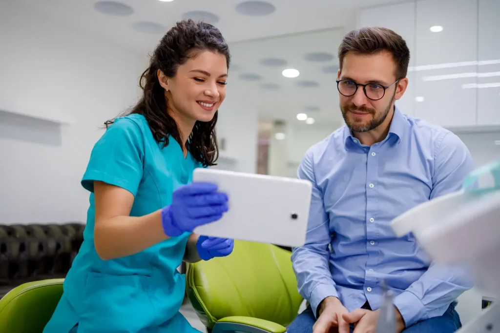 Female dental professional showing a male patient his treatment plan on a digital tablet in a modern dental office