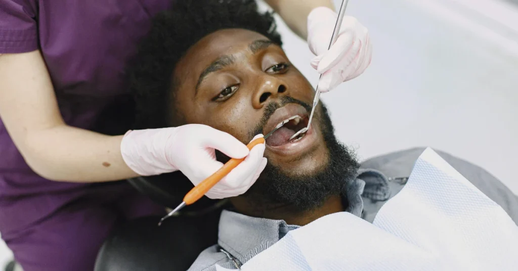 A patient receiving a dental procedure as a dental professional uses tools to treat and examine his teeth during an in-office appointment.